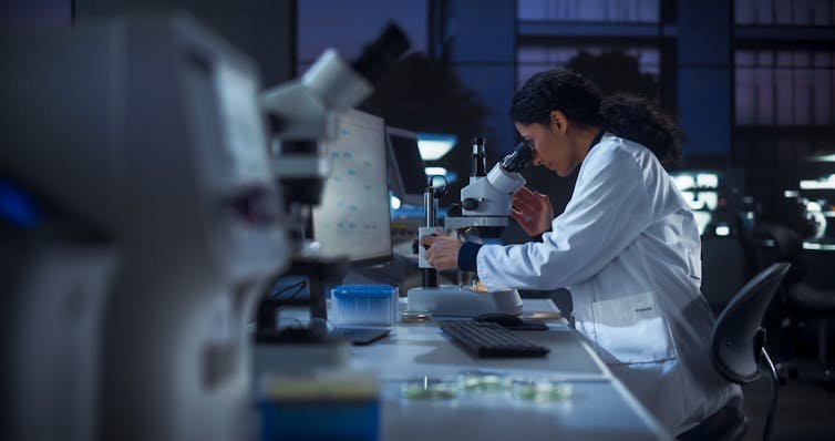 Scientist looking into microscope, surrounded by other lab equipment